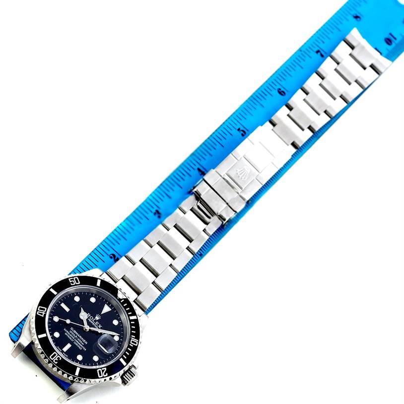 The image shows a Rolex Submariner 16610 Men
s Stainless Steel Black Dial 16610 Men
s Stainless Steel Black Dial watch laid flat next to a blue ruler, displaying the watch face and band.