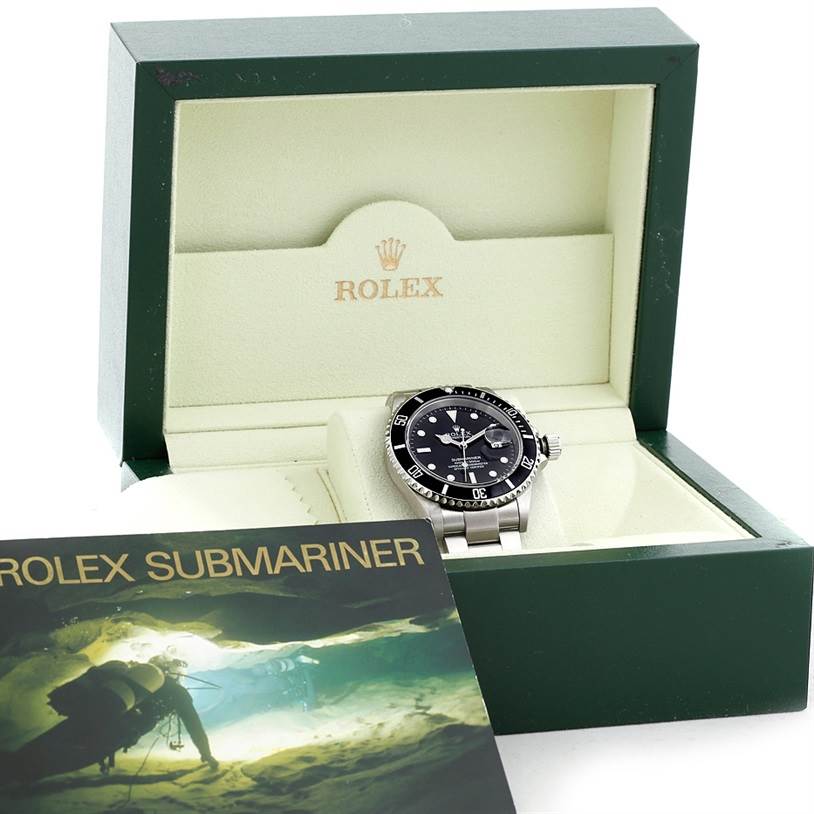 The Rolex Submariner 16610 Men
s Stainless Steel Black Dial 16610 Men
s Stainless Steel Black Dial watch is shown at an angle inside its open green box, with its booklet in the foreground.