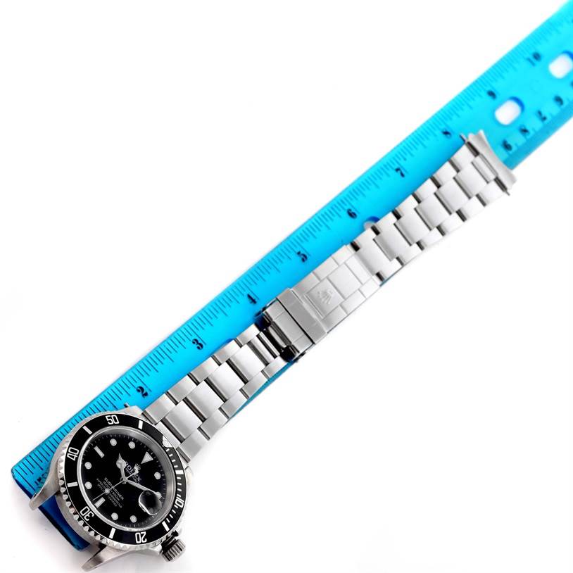 This image shows a top view of the Rolex Submariner 16610 Men
s Stainless Steel Black Dial 16610 Men
s Stainless Steel Black Dial watch with a metal bracelet placed alongside a blue ruler.