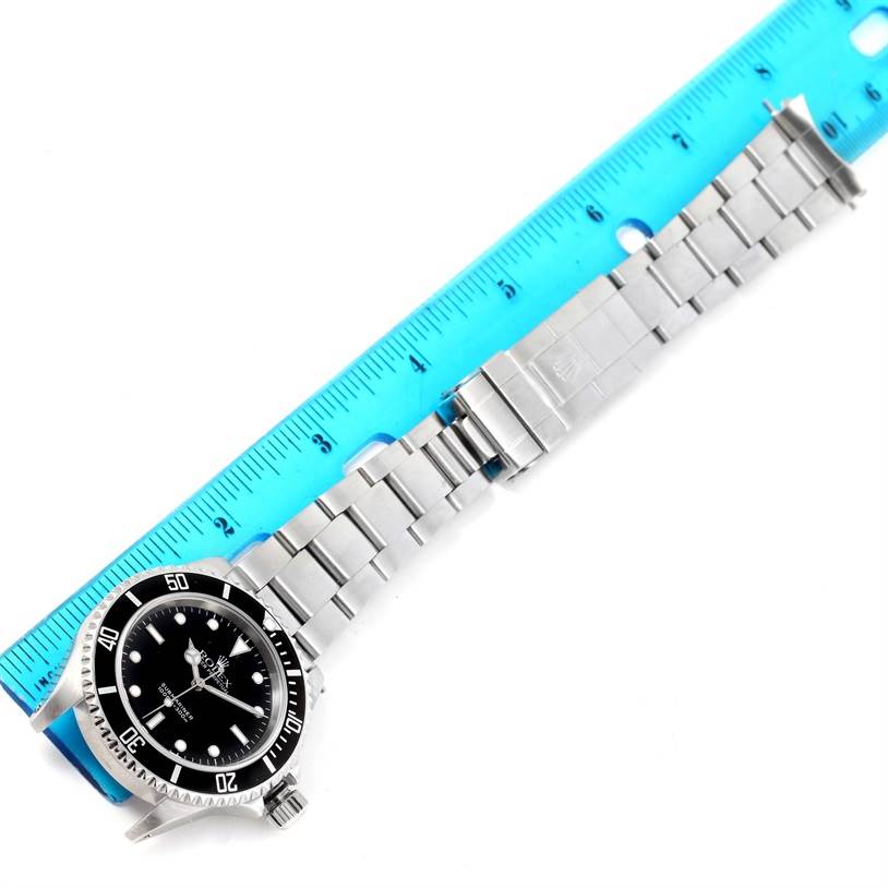 This image shows a top view of a Rolex Submariner 14060 Men
s Stainless Steel Black Dial 14060 Men
s Stainless Steel Black Dial watch with its stainless steel bracelet, next to a blue ruler.