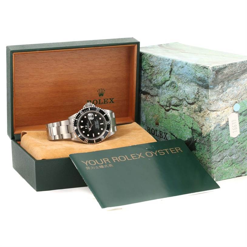 The image shows a Rolex Submariner 16610 Men
s Stainless Steel Black Dial 16610 Men
s Stainless Steel Black Dial watch in its open box with a booklet and outer box visible.