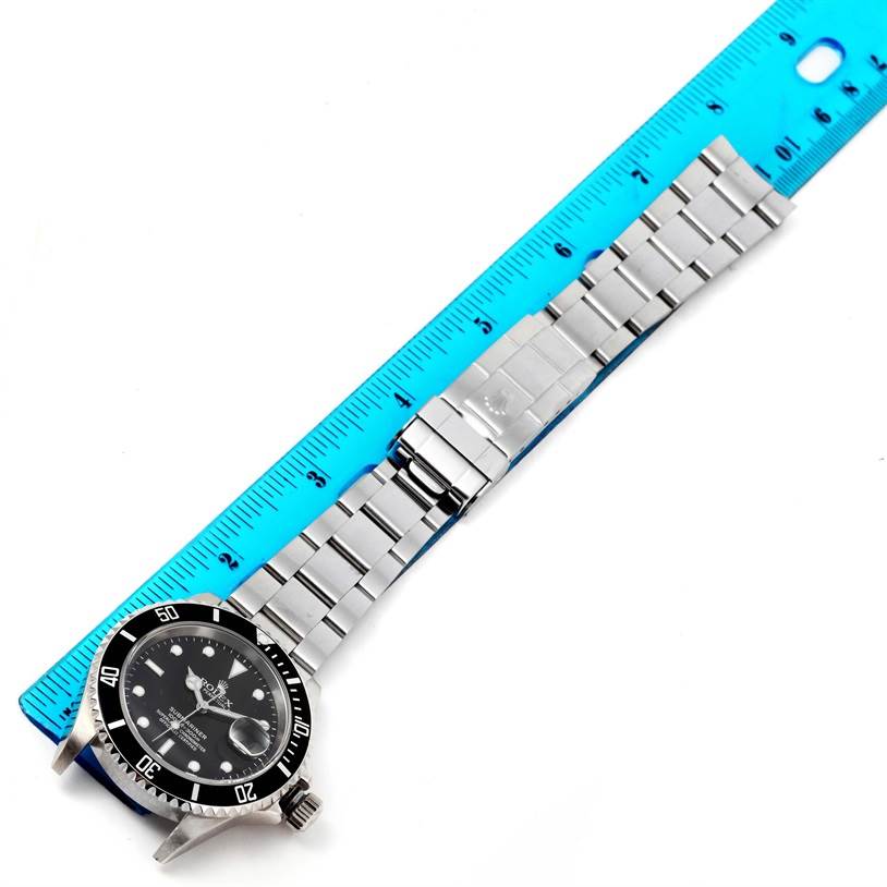 The image shows a Rolex Submariner 16610 Men
s Stainless Steel Black Dial 16610 Men
s Stainless Steel Black Dial watch laid flat next to a blue ruler, displaying the face and stainless steel bracelet.