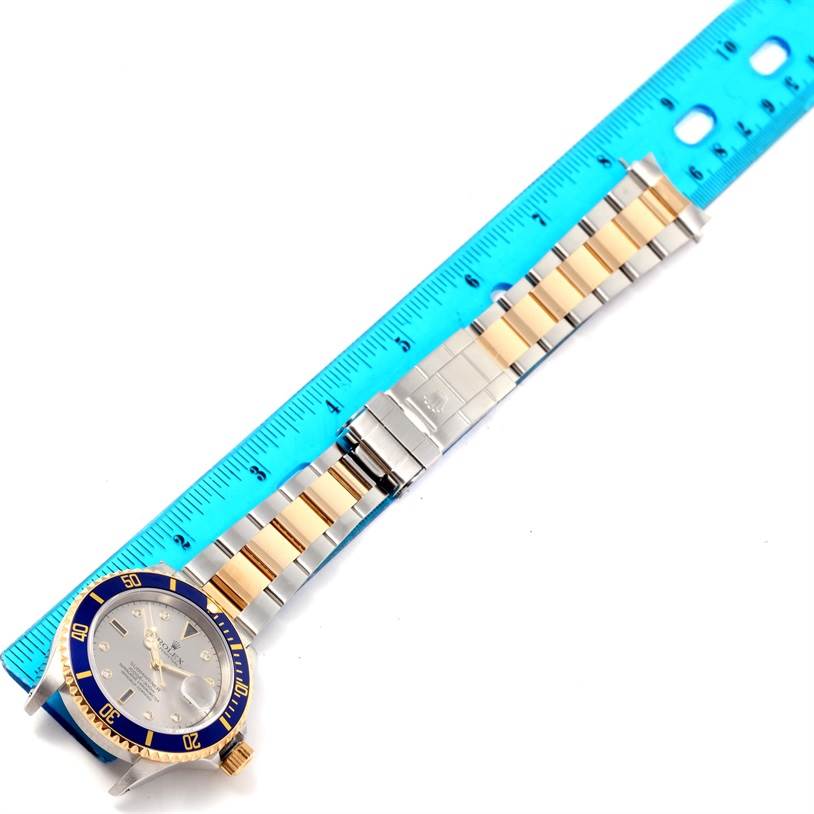 The image shows a top-down view of a Rolex Submariner 16613 Men's Steel and Gold (two tone) Grey Dial 16613 Men's Steel and Gold (two tone) Grey Dial watch, focusing on the face, bezel, and stainless steel and gold bracelet next to a ruler.