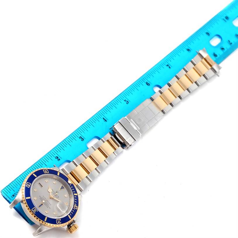 This image shows the Rolex Submariner 16613 Men's Steel and Gold (two tone) Grey Dial 16613 Men's Steel and Gold (two tone) Grey Dial watch laid out flat with a ruler for scale, featuring the face, bezel, and strap.