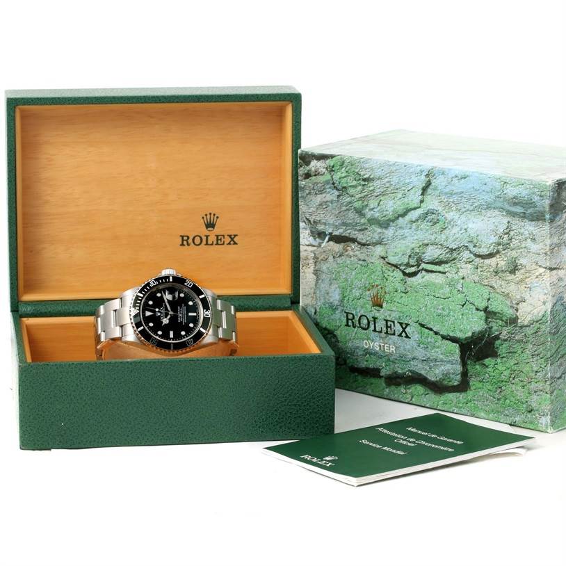 This image shows a Rolex Submariner 16610 Men
s Stainless Steel Black Dial 16610 Men
s Stainless Steel Black Dial watch angled inside an open green box, with its outer box and documents beside it.