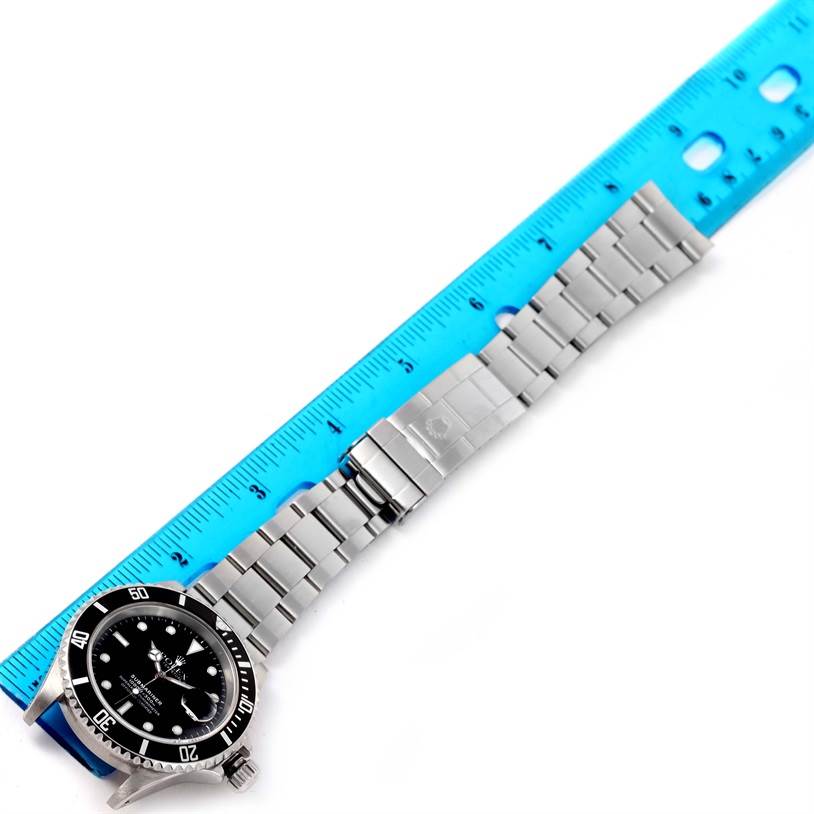 The image shows a Rolex Submariner 16610 Men
s Stainless Steel Black Dial 16610 Men
s Stainless Steel Black Dial watch and its stainless steel bracelet, with a blue ruler next to it for measurement.