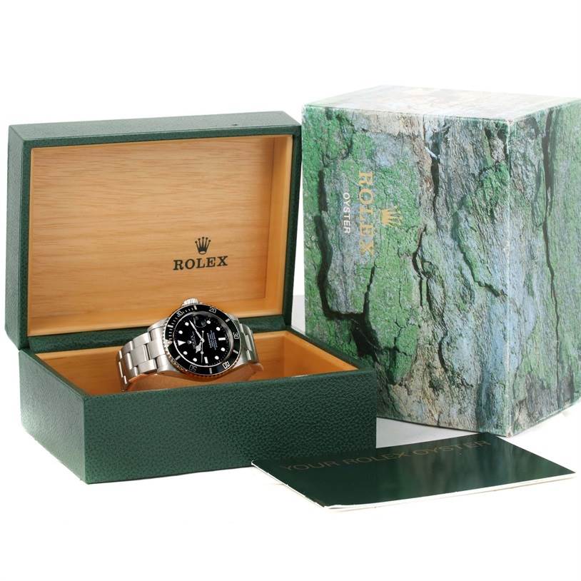 The image shows a Rolex Submariner 16610 Men
s Stainless Steel Black Dial 16610 Men
s Stainless Steel Black Dial watch positioned inside its branded green and wooden box, with its packaging and booklet nearby.