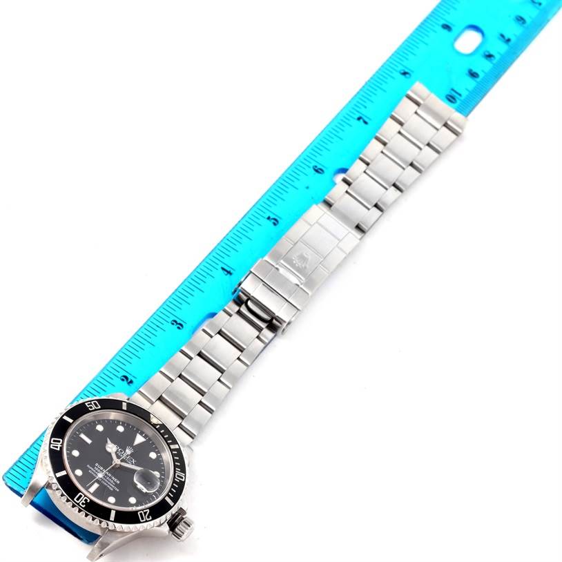 This image shows a Rolex Submariner 16610 Men
s Stainless Steel Black Dial 16610 Men
s Stainless Steel Black Dial watch with a blue ruler measuring its bracelet, displayed from an overhead angle.