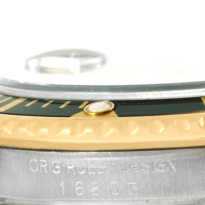 The image shows a close-up side view of the Rolex Submariner 16803 Men
s Steel and Gold (two tone) Black Dial 16803 Men
s Steel and Gold (two tone) Black Dial, highlighting its bezel and engraved model number.