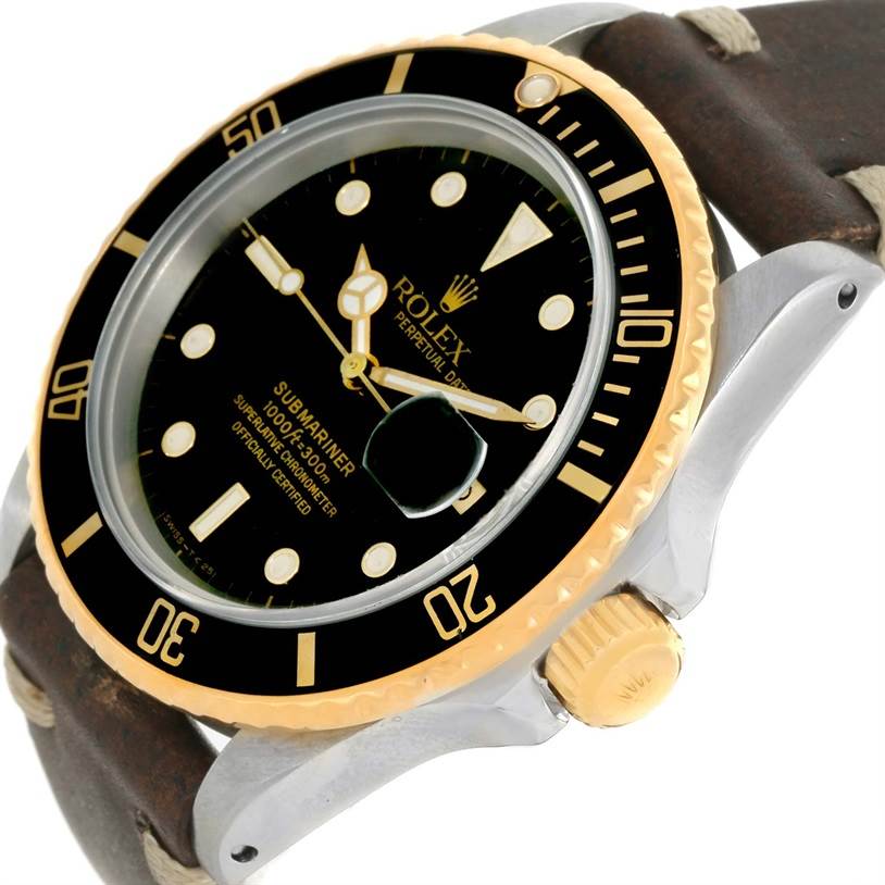 This image shows a side angle of a Rolex Submariner 16803 Men
s Steel and Gold (two tone) Black Dial 16803 Men
s Steel and Gold (two tone) Black Dial watch, highlighting its bezel, dial, and crown with a brown strap.