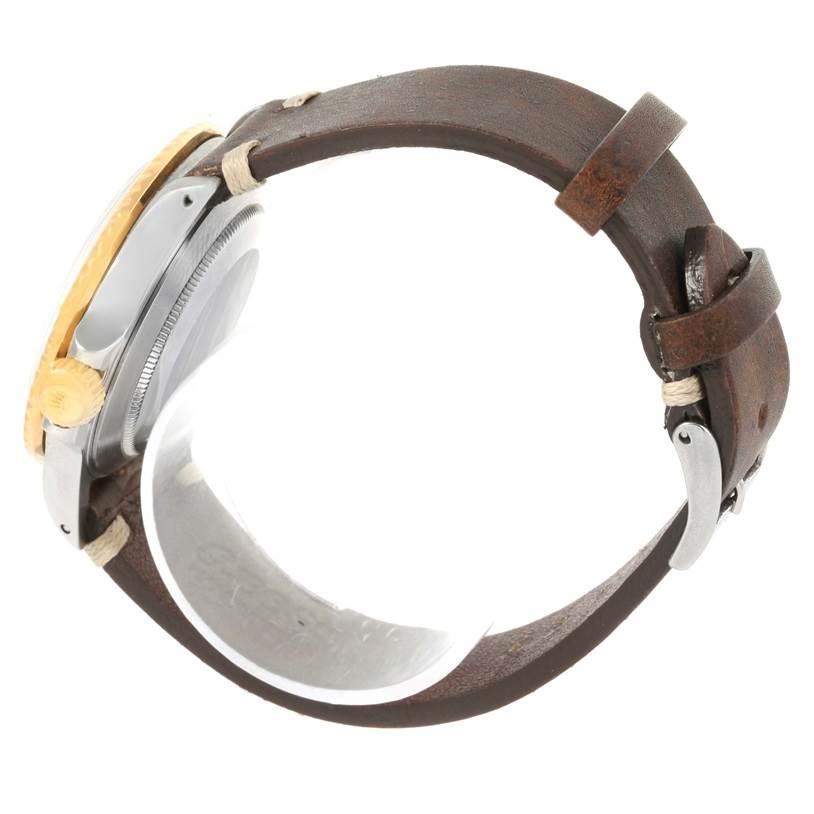 The Rolex Submariner 16803 Men
s Steel and Gold (two tone) Black Dial 16803 Men
s Steel and Gold (two tone) Black Dial watch is shown side-on with a focus on its bezel, crown, case, and leather strap.