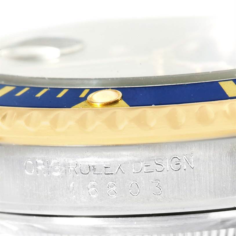 This image shows a close-up angle of the blue and gold bezel and part of the case with engraving on a Rolex Submariner 16803 Men
s Steel and Gold (two tone) Blue Dial 16803 Men
s Steel and Gold (two tone) Blue Dial watch.