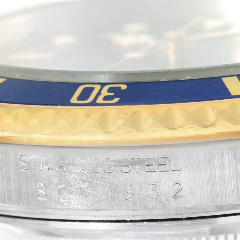 The image shows a close-up of the side of a Rolex Submariner 16803 Men
s Steel and Gold (two tone) Blue Dial 16803 Men
s Steel and Gold (two tone) Blue Dial, highlighting the bezel and case with "STAINLESS STEEL" and serial number.
