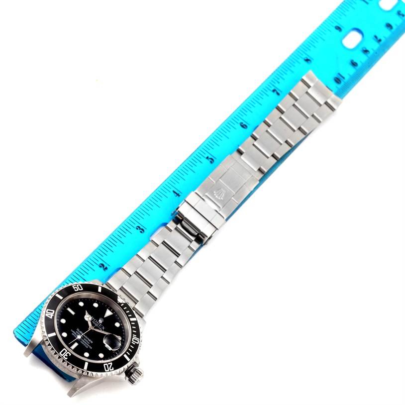 The Rolex Submariner 16610 Men
s Stainless Steel Black Dial 16610 Men
s Stainless Steel Black Dial watch is shown laying flat, with the face, bracelet, and clasp visible against a ruler.