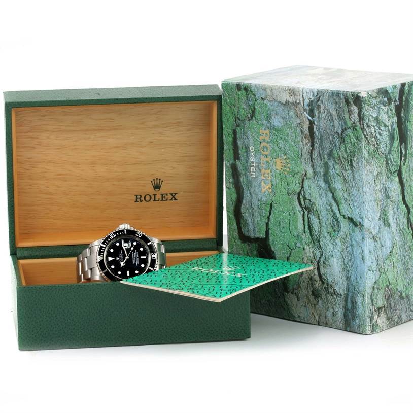 A Rolex Submariner 16610 Men
s Stainless Steel Black Dial 16610 Men
s Stainless Steel Black Dial watch is shown partially inside its green and wooden box, with green accessories next to it.
