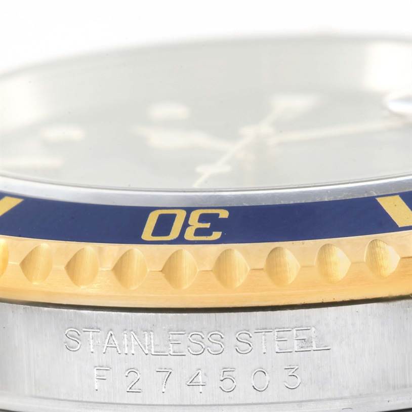 This close-up shot of the Rolex Submariner 16613 Men's Steel and Gold (two tone) Blue Dial 16613 Men's Steel and Gold (two tone) Blue Dial shows the bezel, part of the dial, and the stainless steel case with a serial number.