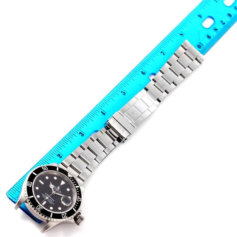 The image shows a Rolex Submariner 16610 Men
s Stainless Steel Black Dial 16610 Men
s Stainless Steel Black Dial watch laid flat with its stainless steel bracelet and clasp extended, next to a ruler for measurement.