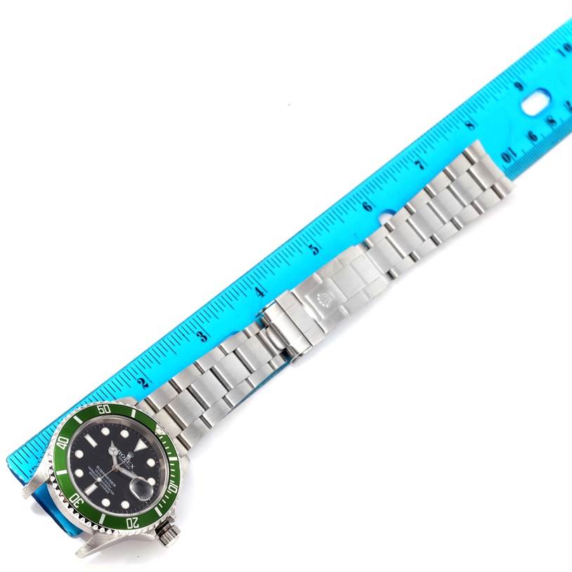 The image shows a Rolex Submariner 16610LV Men
s Stainless Steel Black Dial 16610LV Men
s Stainless Steel Black Dial watch laying flat with its green bezel, bracelet, and deployment clasp visible, measured by a blue ruler.