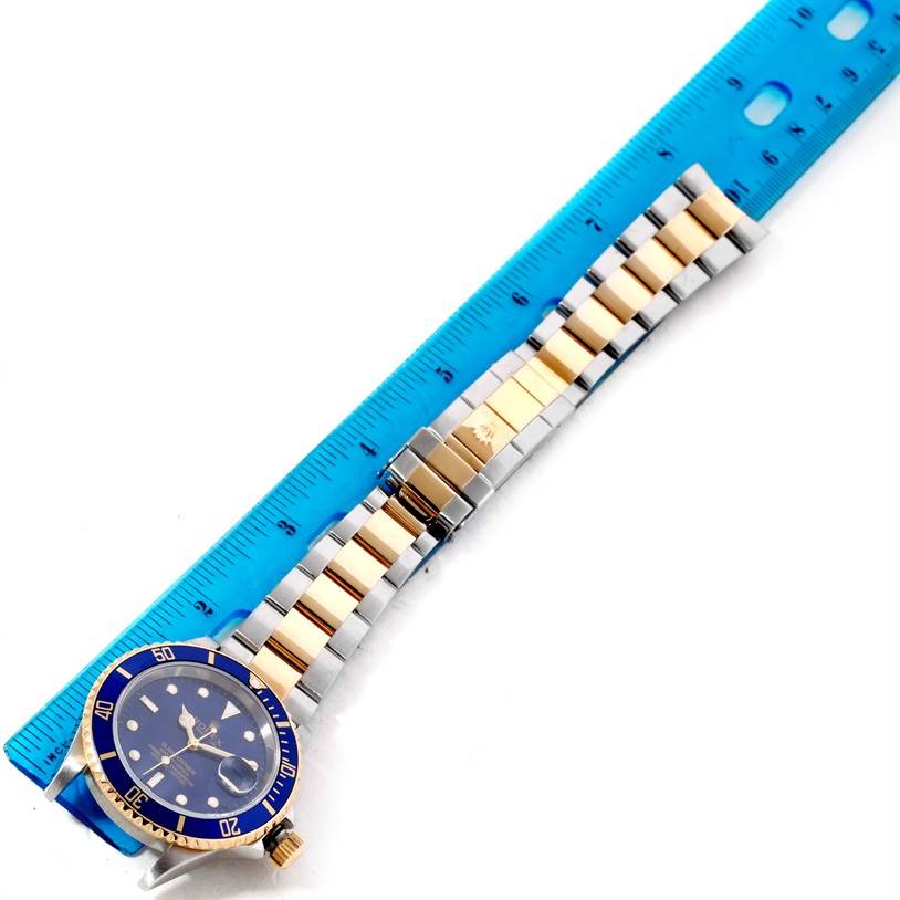 The image shows a Rolex Submariner 16613 Men
s Steel and Gold (two tone) Blue Dial 16613 Men
s Steel and Gold (two tone) Blue Dial watch laid flat against a blue ruler, displaying the face, bezel, and bracelet from the top-down angle.