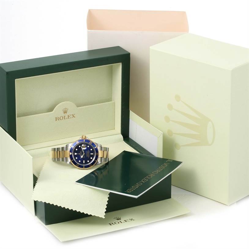 The image shows a Rolex Submariner 16613 Men's Steel and Gold (two tone) Blue Dial 16613 Men's Steel and Gold (two tone) Blue Dial watch with a blue dial and two-tone bracelet, displayed in its original box with accompanying accessories.