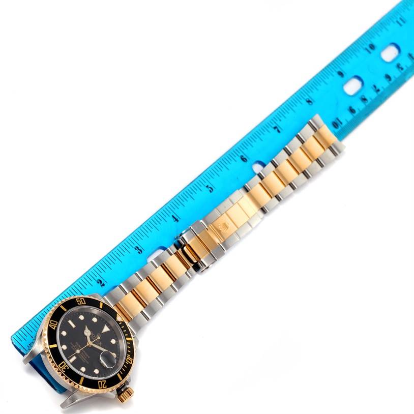 The image shows a top view of a Rolex Submariner 16613 Men's Steel and Gold (two tone) Black Dial 16613 Men's Steel and Gold (two tone) Black Dial watch with its dial, bezel, and bracelet placed next to a ruler.