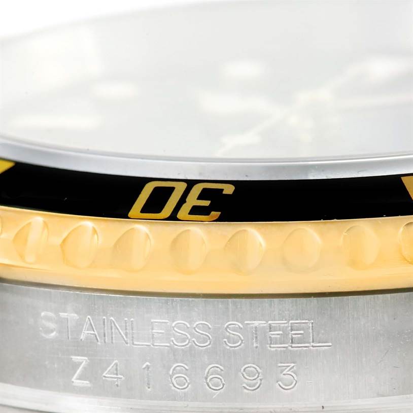 Close-up of the Rolex Submariner 16613 Men's Steel and Gold (two tone) Black Dial 16613 Men's Steel and Gold (two tone) Black Dial watch bezel and part of the case, displaying "STAINLESS STEEL" and the serial number.
