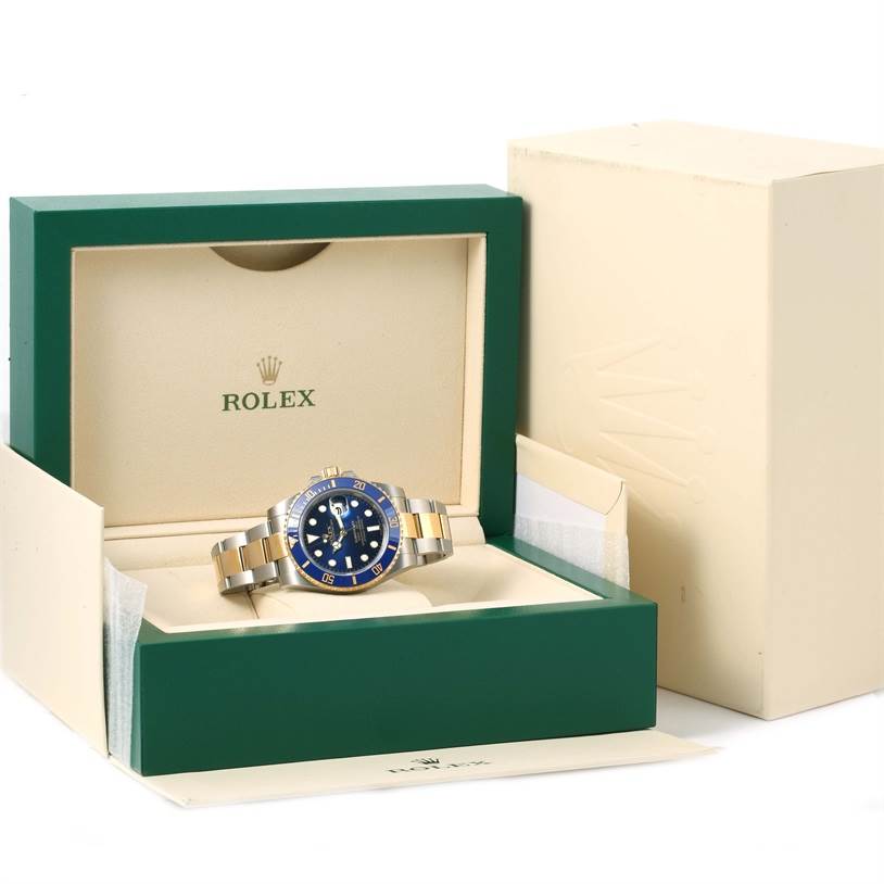 The Rolex Submariner 116613 Men's Steel and Gold (two tone) Blue Dial 116613 Men's Steel and Gold (two tone) Blue Dial is shown at an angle inside its green and cream-colored box with its bracelet and bezel visible.