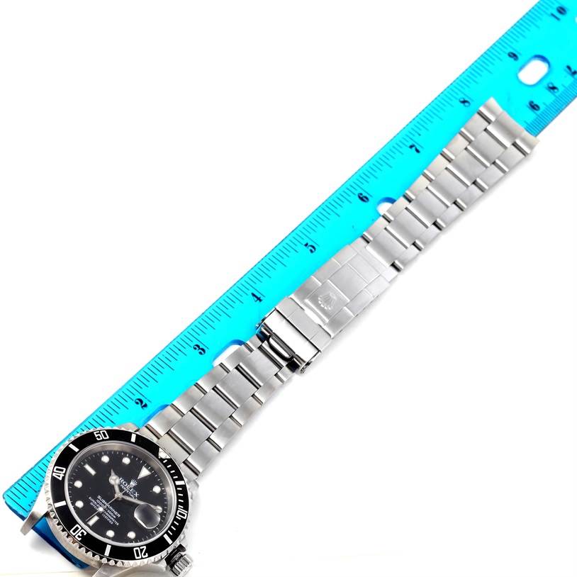 The image shows a Rolex Submariner 16610 Men
s Stainless Steel Black Dial 16610 Men
s Stainless Steel Black Dial watch laid flat next to a ruler, displaying its face, bezel, and metal bracelet.