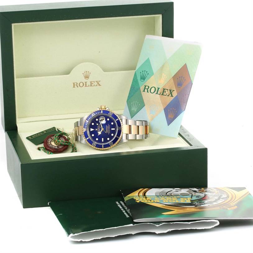 A Rolex Submariner 16613 Men's Steel and Gold (two tone) Blue Dial 16613 Men's Steel and Gold (two tone) Blue Dial watch with a blue dial is displayed in an open green Rolex box alongside its accessories and booklets.
