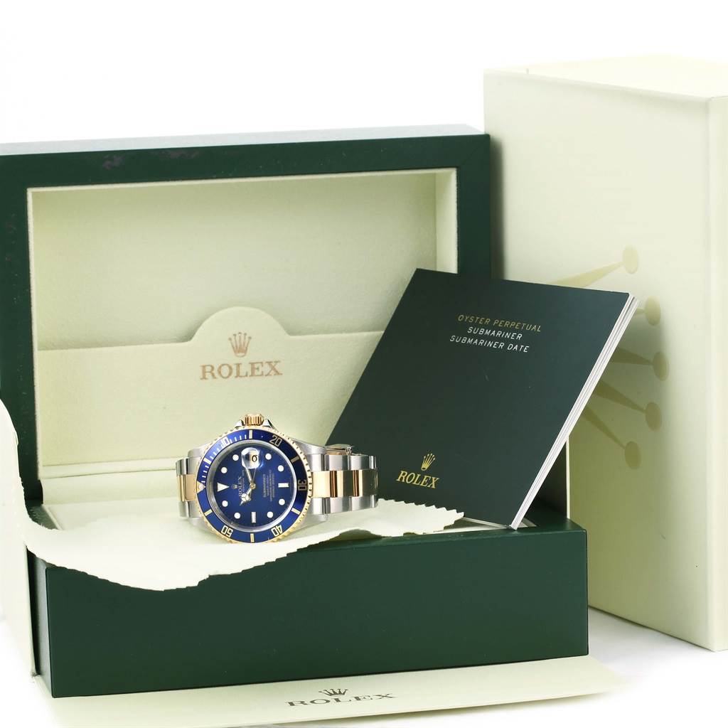 The image shows a Rolex Submariner 16613 Men
s Steel and Gold (two tone) Blue Dial 16613 Men
s Steel and Gold (two tone) Blue Dial watch in its case along with the booklet and packaging, viewed from the front.