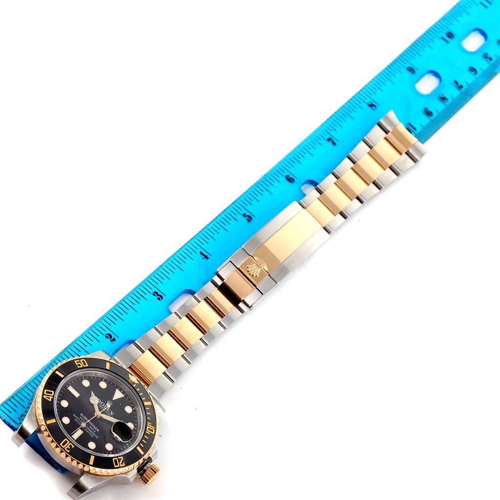 The image shows a Rolex Submariner 116613LN Men
s Steel and Gold (two tone) Black Dial 116613LN Men
s Steel and Gold (two tone) Black Dial watch face and full bracelet, placed alongside a blue ruler for measurement.