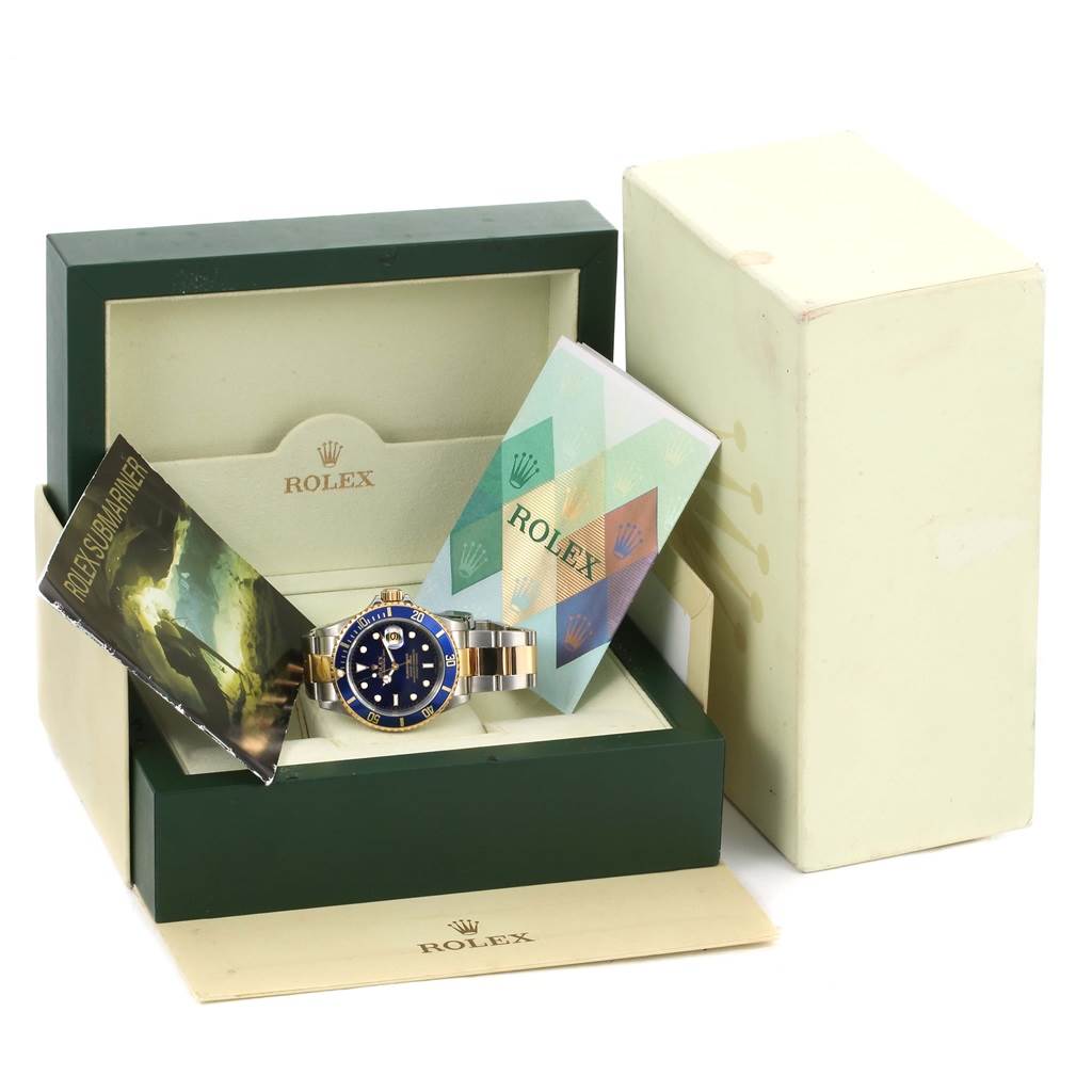 The image shows a Rolex Submariner 16613 Men
s Steel and Gold (two tone) Blue Dial 16613 Men
s Steel and Gold (two tone) Blue Dial watch with its box, manuals, and original packaging from a frontal angle.