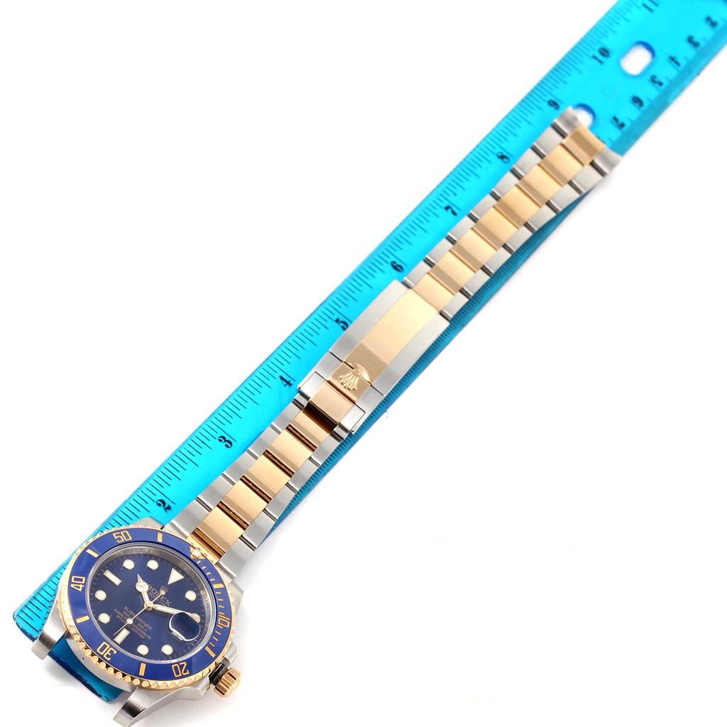 This image shows a top-down view of a Rolex Submariner 116613 Men
s Steel and Gold (two tone) Blue Dial 116613 Men
s Steel and Gold (two tone) Blue Dial watch aligned next to a blue ruler, displaying the watch
s bezel, dial, and bracelet.