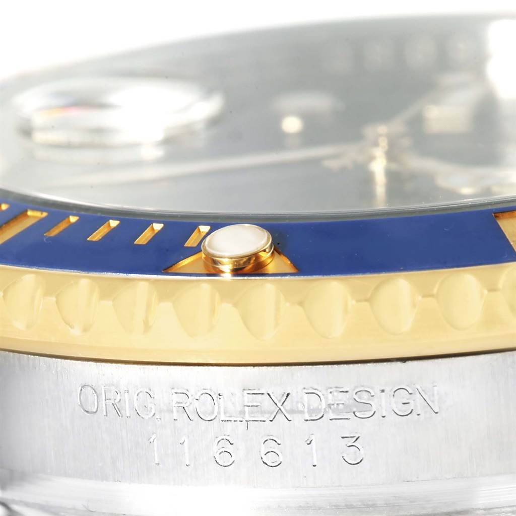 This close-up image of a Rolex Submariner 116613 Men
s Steel and Gold (two tone) Blue Dial 116613 Men
s Steel and Gold (two tone) Blue Dial watch showcases the bezel, part of the crystal, and the engraved case with the model number.