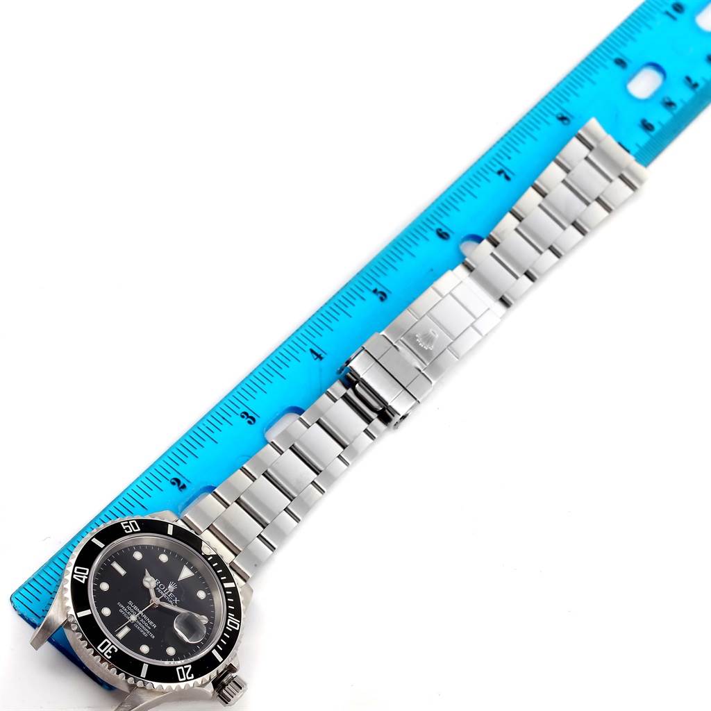 The image shows a top-down view of a Rolex Submariner 16610 Men
s Stainless Steel Black Dial 16610 Men
s Stainless Steel Black Dial watch laid next to a blue ruler.