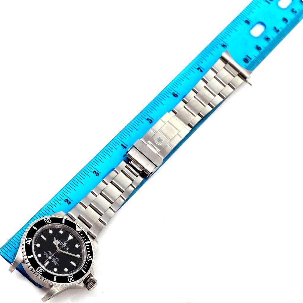 The Rolex Submariner 14060 Men
s Stainless Steel Black Dial 14060 Men
s Stainless Steel Black Dial watch is shown laying flat next to a ruler, displaying its face, bezel, bracelet, and clasp.