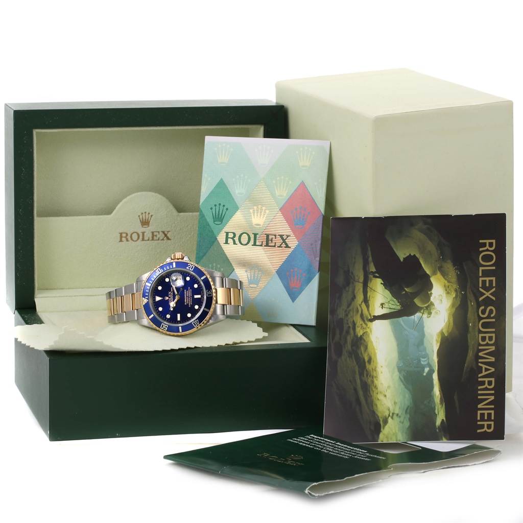 The image shows a Rolex Submariner 16613 Men
s Steel and Gold (two tone) Blue Dial 16613 Men
s Steel and Gold (two tone) Blue Dial watch along with its box, manuals, and additional packaging.