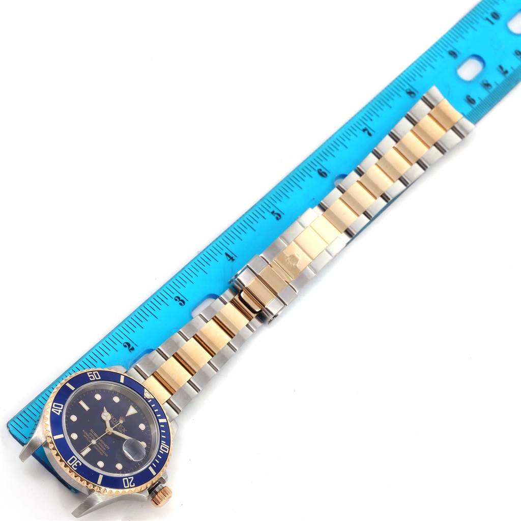 The image shows a Rolex Submariner 16613 Men
s Steel and Gold (two tone) Blue Dial 16613 Men
s Steel and Gold (two tone) Blue Dial watch laid flat, with the face and bracelet fully visible next to a blue ruler.