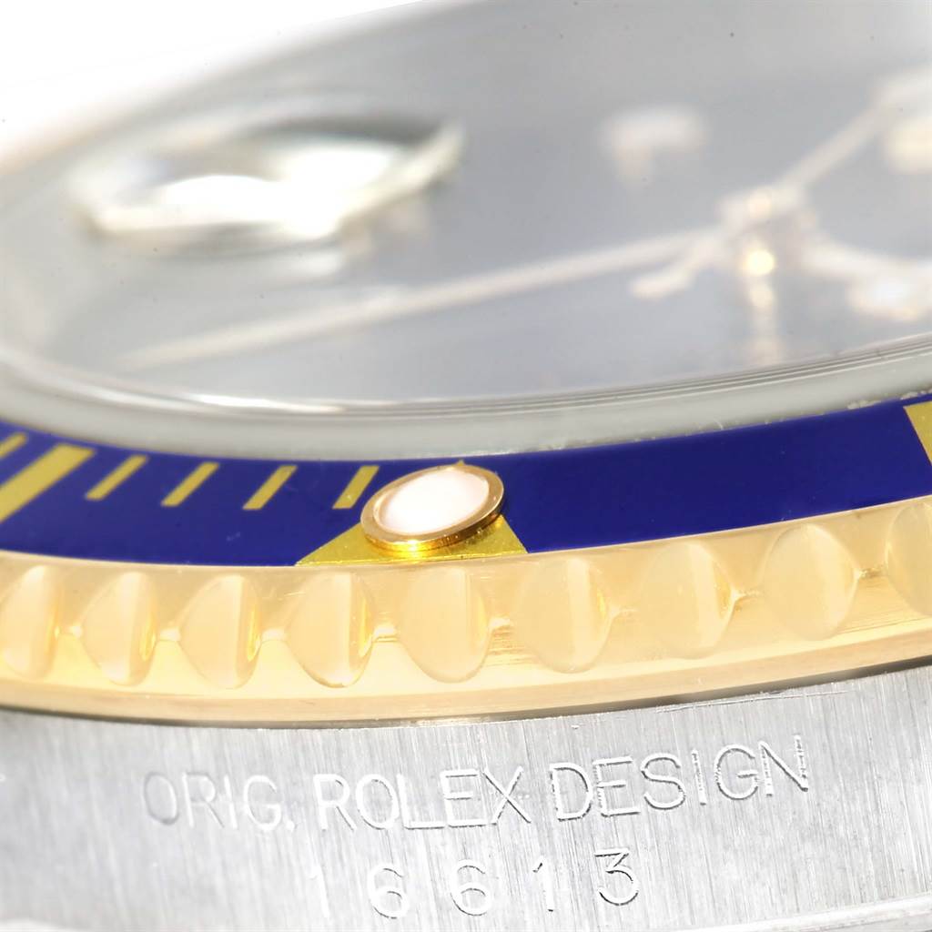 This close-up angle of the Rolex Submariner 16613 Men's Steel and Gold (two tone) Blue Dial 16613 Men's Steel and Gold (two tone) Blue Dial watch shows the bezel, sapphire crystal, and part of the case with engraved text.