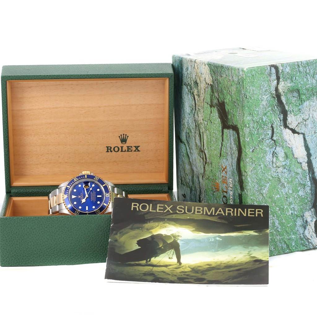 The image shows a Rolex Submariner 16613 Men's Steel and Gold (two tone) Blue Dial 16613 Men's Steel and Gold (two tone) Blue Dial watch, its open green box, and its booklet displayed from a front angle.