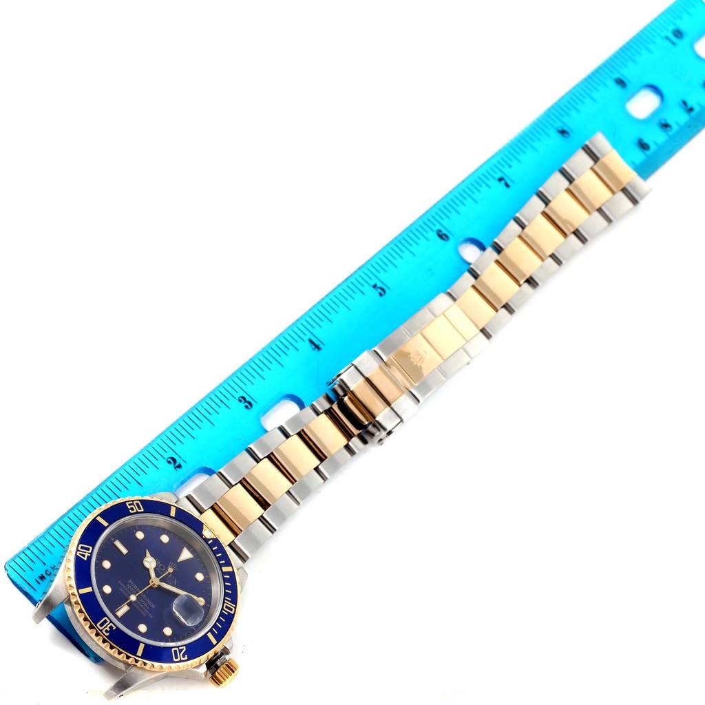 The Rolex Submariner 16613 Men's Steel and Gold (two tone) Blue Dial 16613 Men's Steel and Gold (two tone) Blue Dial watch is shown from a top-down angle, displaying its face, bezel, and bracelet alongside a ruler for scale.