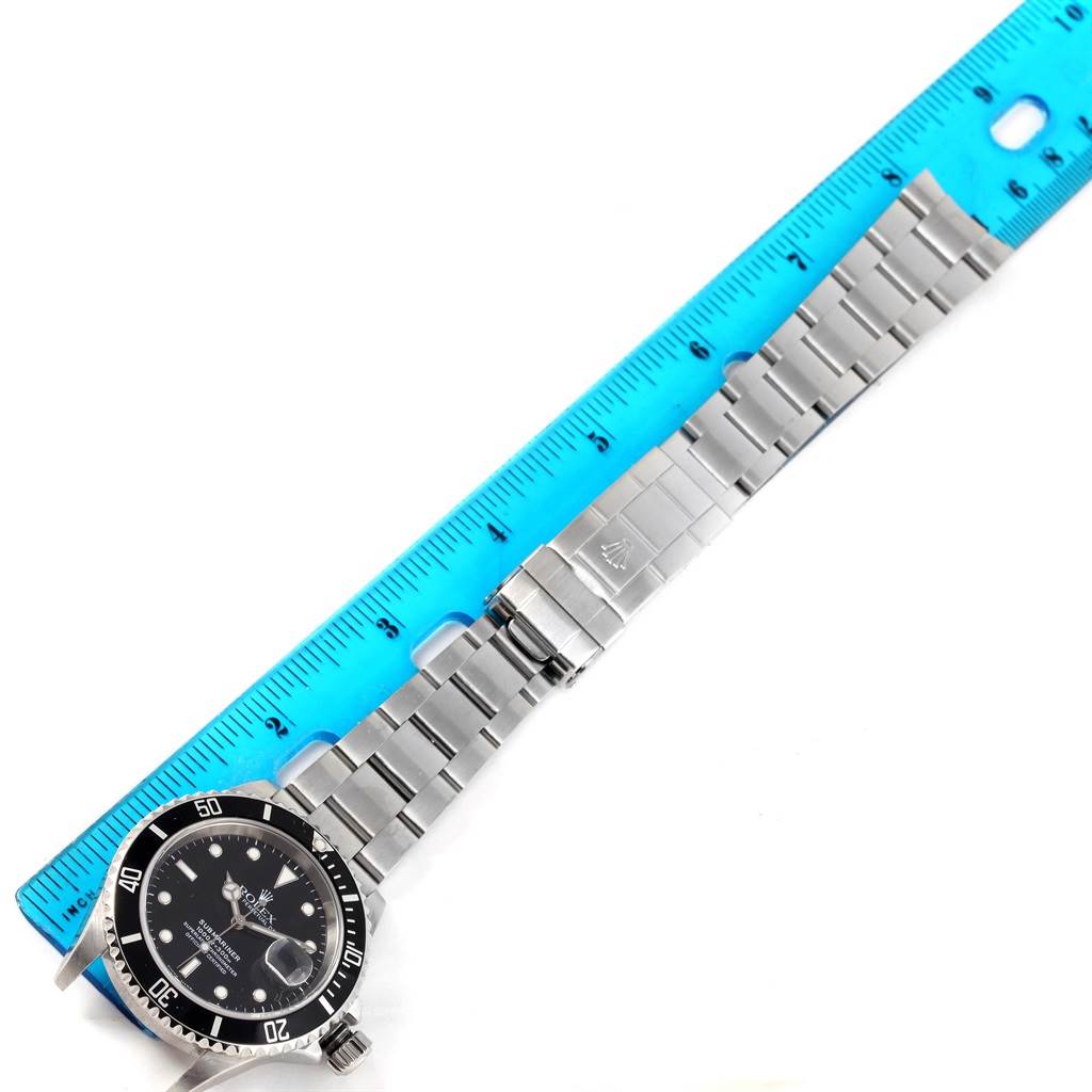 The image shows a top view of a Rolex Submariner 16610 Men
s Stainless Steel Black Dial 16610 Men
s Stainless Steel Black Dial watch, focusing on the watch
s face, bezel, and bracelet alongside a ruler.