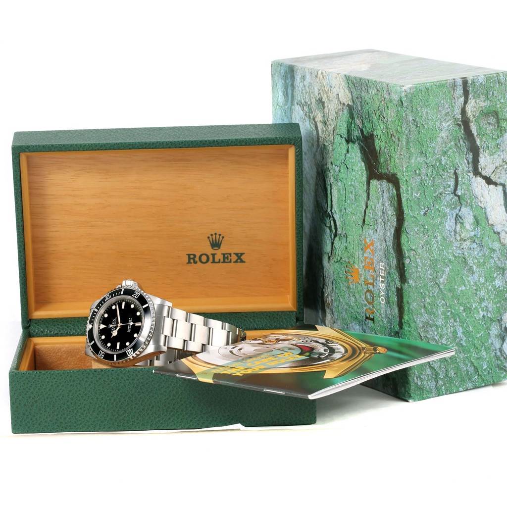 The Rolex Submariner 14060 Men
s Stainless Steel Black Dial 14060 Men
s Stainless Steel Black Dial watch is shown at an angle within its open box, next to its outer box and booklet.