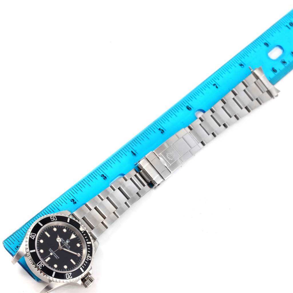 The Rolex Submariner 14060 Men
s Stainless Steel Black Dial 14060 Men
s Stainless Steel Black Dial watch is shown flat with its face, stainless steel bracelet, and clasp alongside a blue ruler for scale.