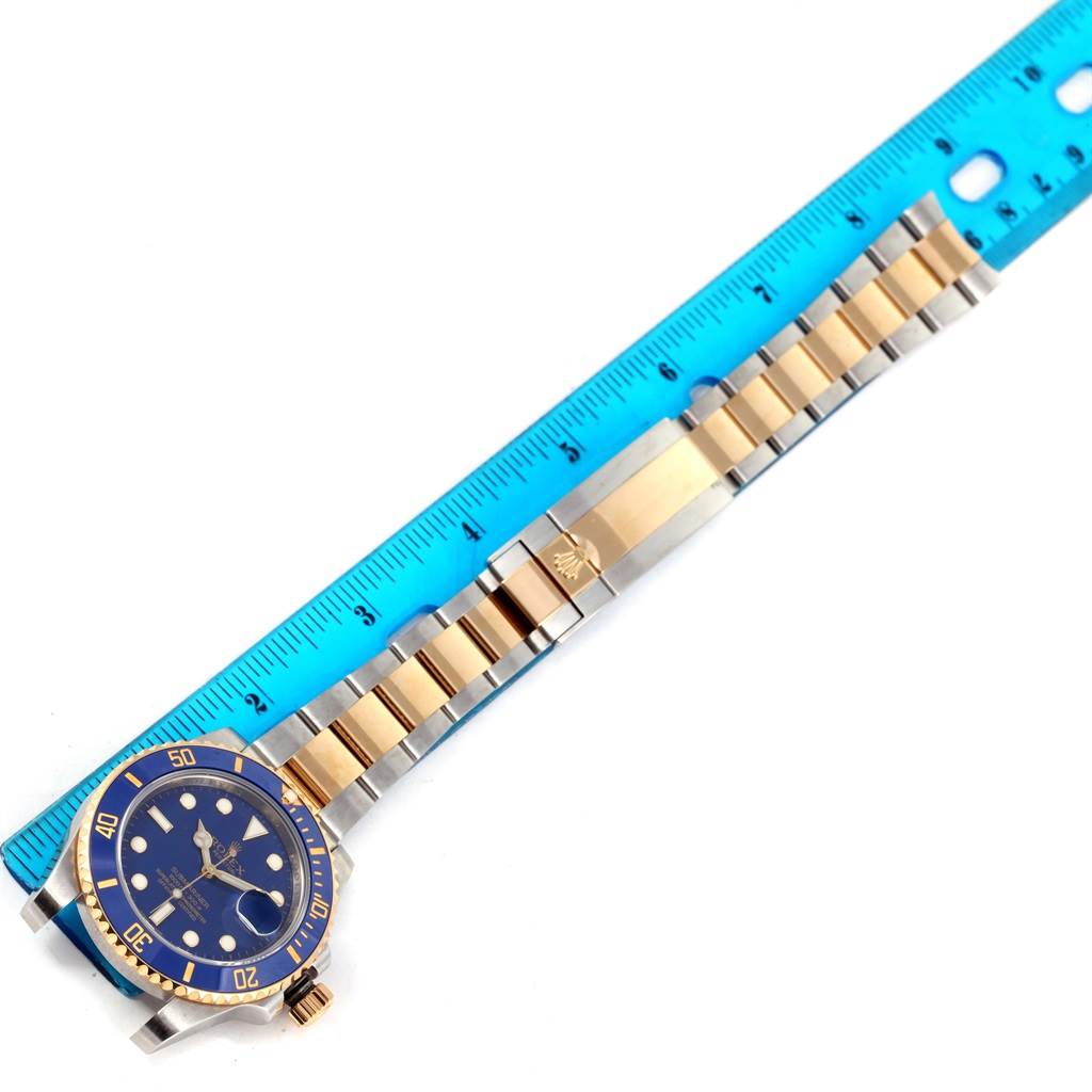 The image shows a Rolex Submariner 116613 Men
s Steel and Gold (two tone) Blue Dial 116613 Men
s Steel and Gold (two tone) Blue Dial watch laid flat next to a ruler, emphasizing the two-tone metal bracelet and blue dial.