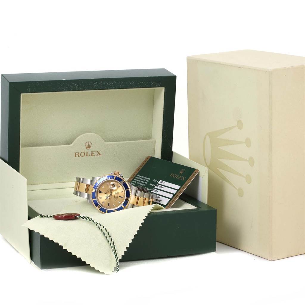 The Rolex Submariner 16613 Men's Steel and Gold (two tone) Champagne Dial 16613 Men's Steel and Gold (two tone) Champagne Dial watch is pictured at an angle showing its face, strap, and box along with a warranty card and cleaning cloth.