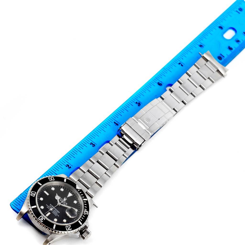 The image shows a Rolex Submariner 16610 Men's Stainless Steel Black Dial 16610 Men's Stainless Steel Black Dial watch laid flat with its bracelet next to a blue ruler for measurement.