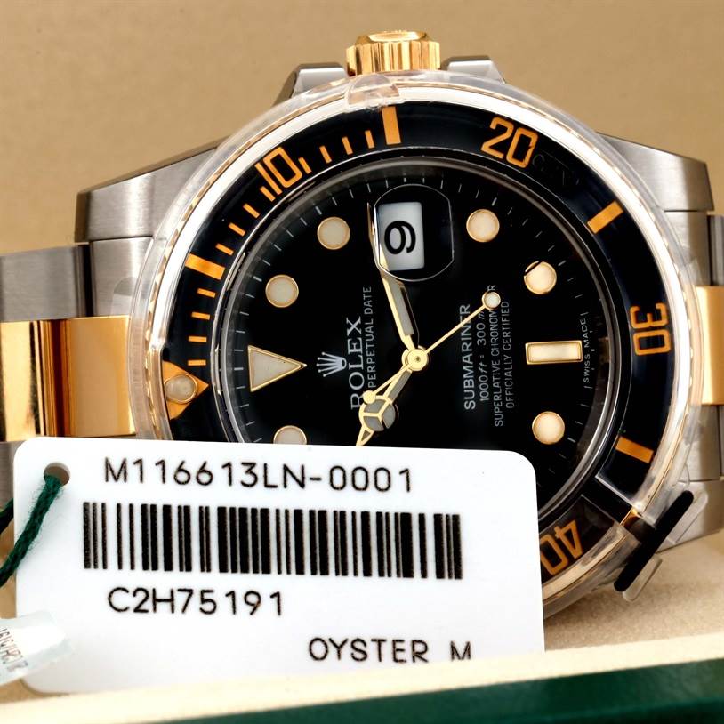 The image shows a close-up angle of a Rolex Submariner 116613LN Men's Steel and Gold (two tone) Black Dial 116613LN Men's Steel and Gold (two tone) Black Dial watch, highlighting its dial, bezel, and part of the bracelet, along with a tag.