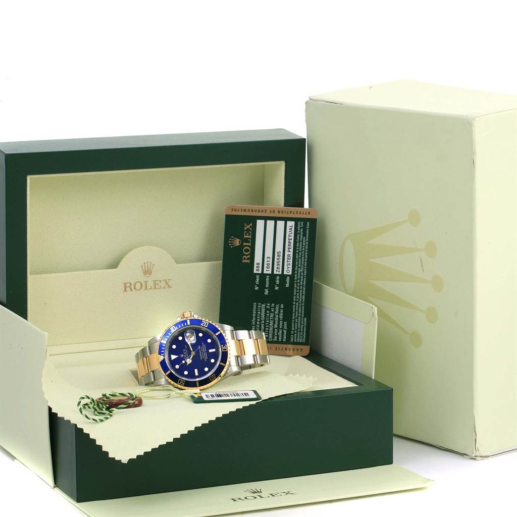 The image shows a Rolex Submariner 16613 Men's Steel and Gold (two tone) Blue Dial 16613 Men's Steel and Gold (two tone) Blue Dial watch in its box, including a warranty card, tag, and the outer packaging.