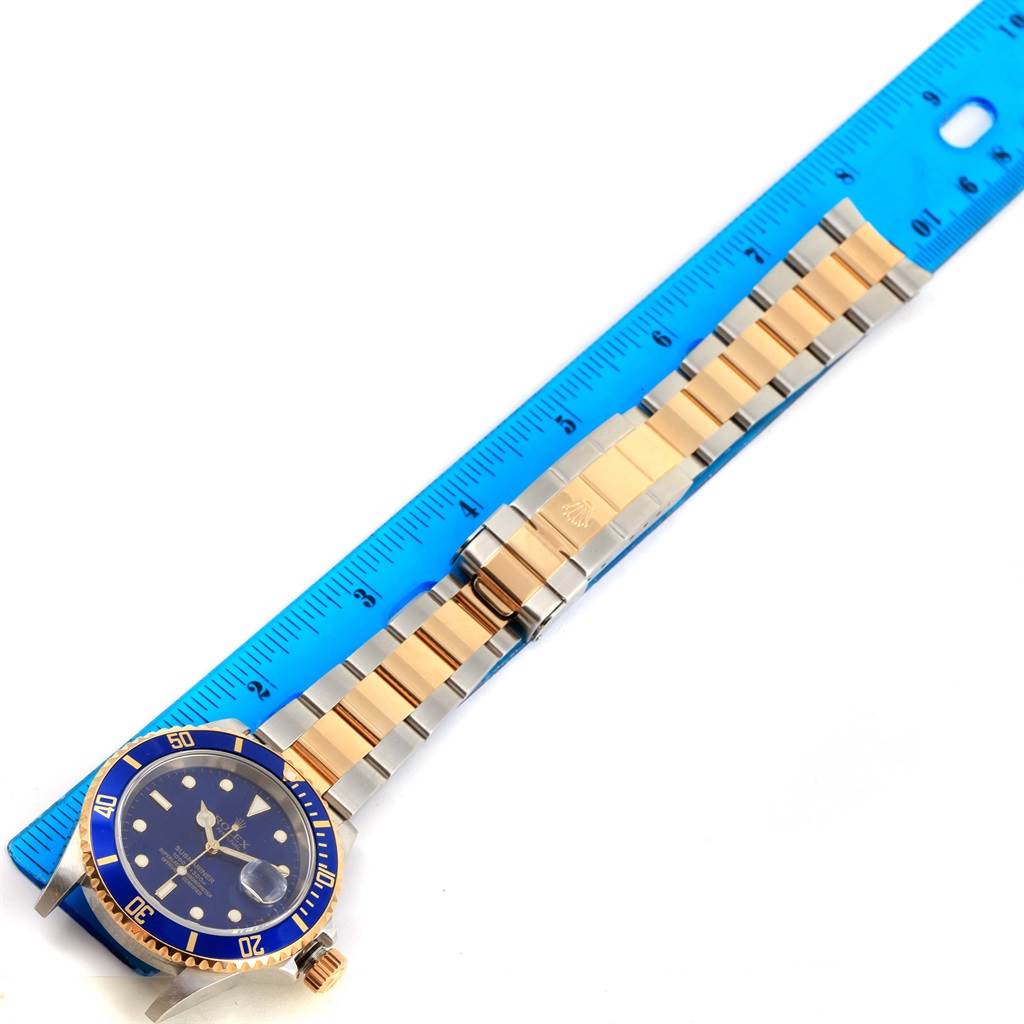 The image shows a Rolex Submariner 16613 Men's Steel and Gold (two tone) Blue Dial 16613 Men's Steel and Gold (two tone) Blue Dial watch at an angled top-down view, highlighting its blue bezel, dial, and gold and silver bracelet.